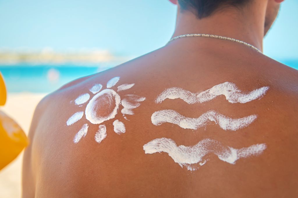 Homem com sol e ondas desenhadas com protetor solar nas costas