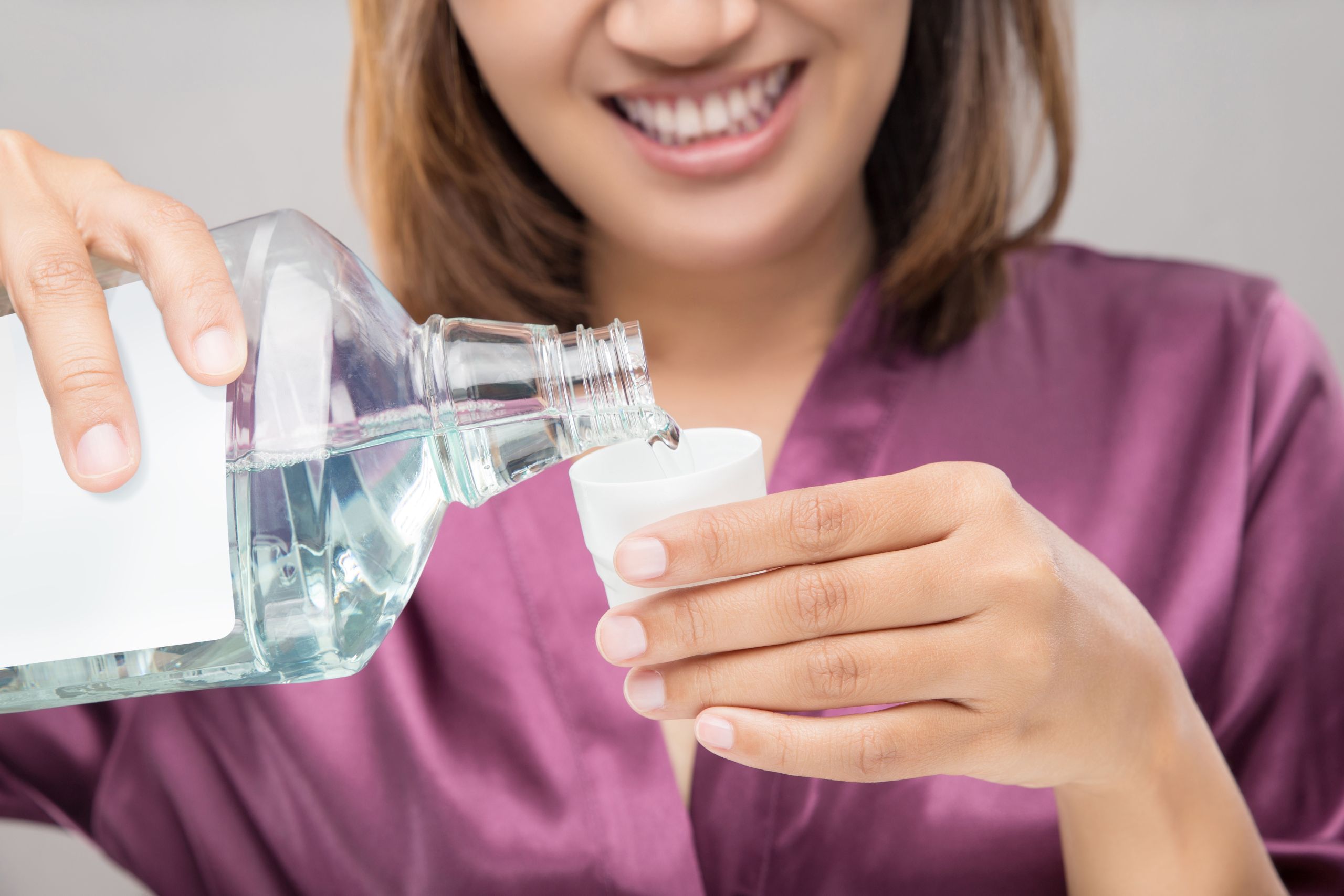 Doença periodontal: como o CBD pode transformar a saúde bucal. Foto de uma mulher colocando enxaguante bucal em uma tampinha e sorrindo